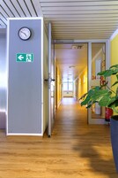Un pasillo con un reloj en la pared, un letrero de salida de emergencia y una planta.