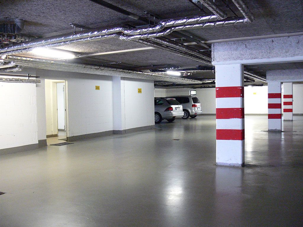 A parking garage with white walls, red and white pillars, and a few parked cars.