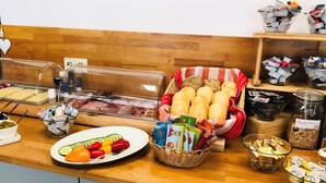 A breakfast buffet with various food items, including bread, pastries, and a plate of sliced vegetables. - Motel Drei König (Heimsheim)
