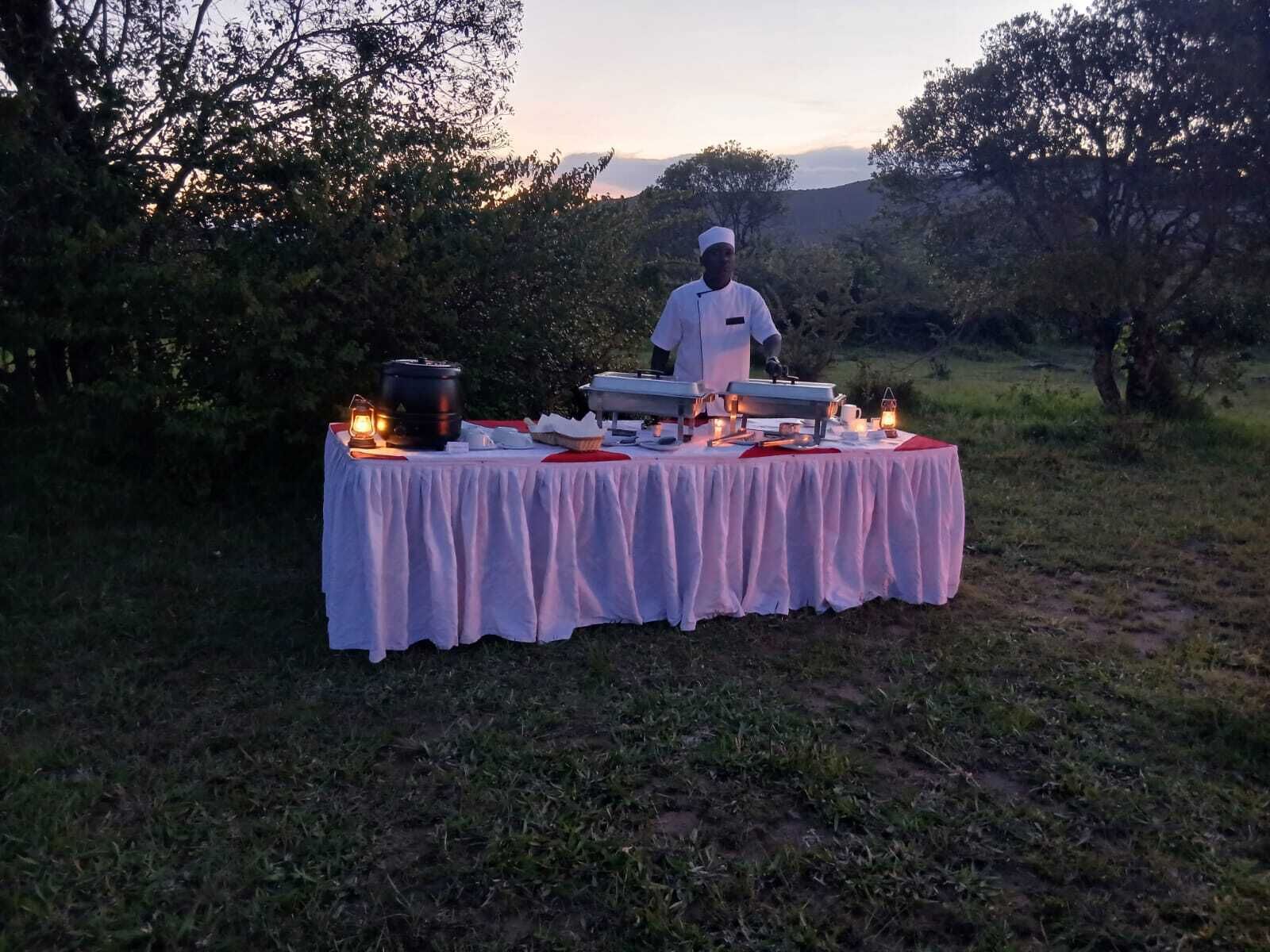 Un chef se tient derrière une table installée à l’extérieur, sur laquelle sont disposés des aliments et du matériel de cuisine.