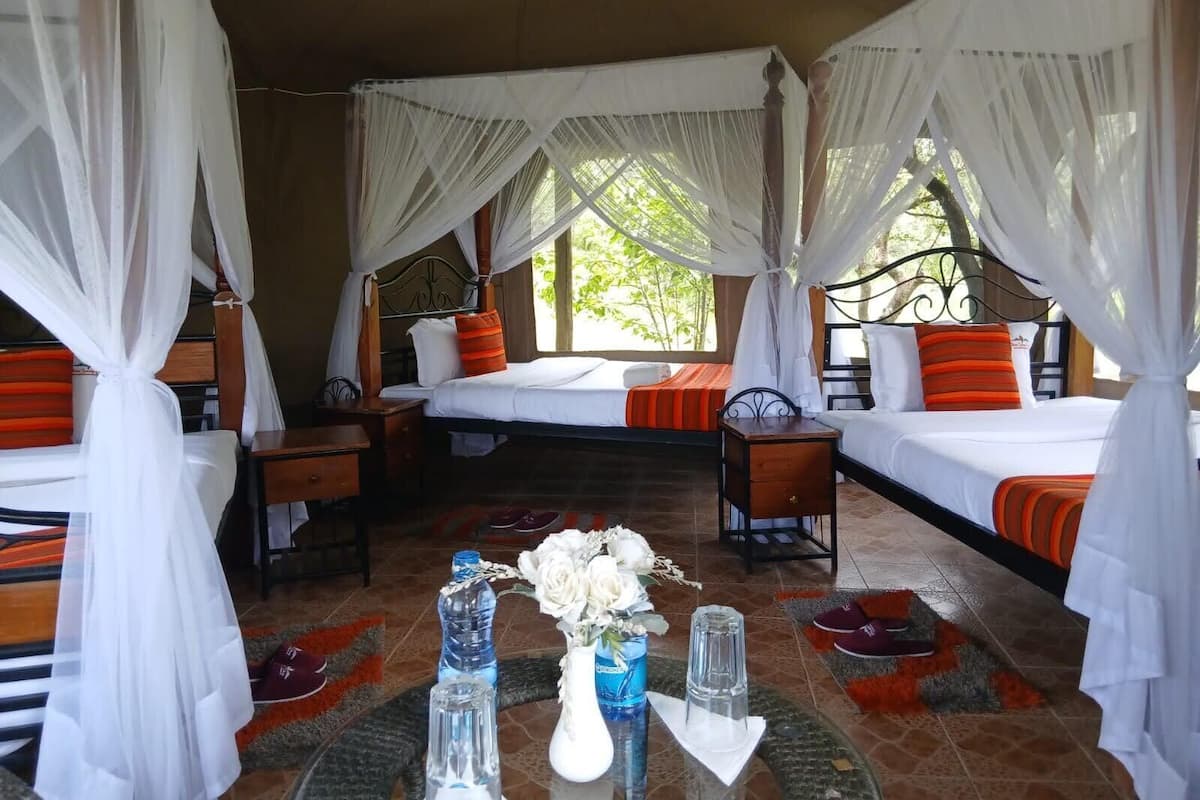 A room with two beds, each with a canopy, a small table with a vase of flowers, and a water bottle.