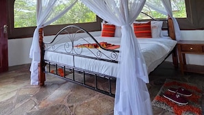 A tent-style room with a bed, a hanging light fixture, and a window with a view of greenery.
