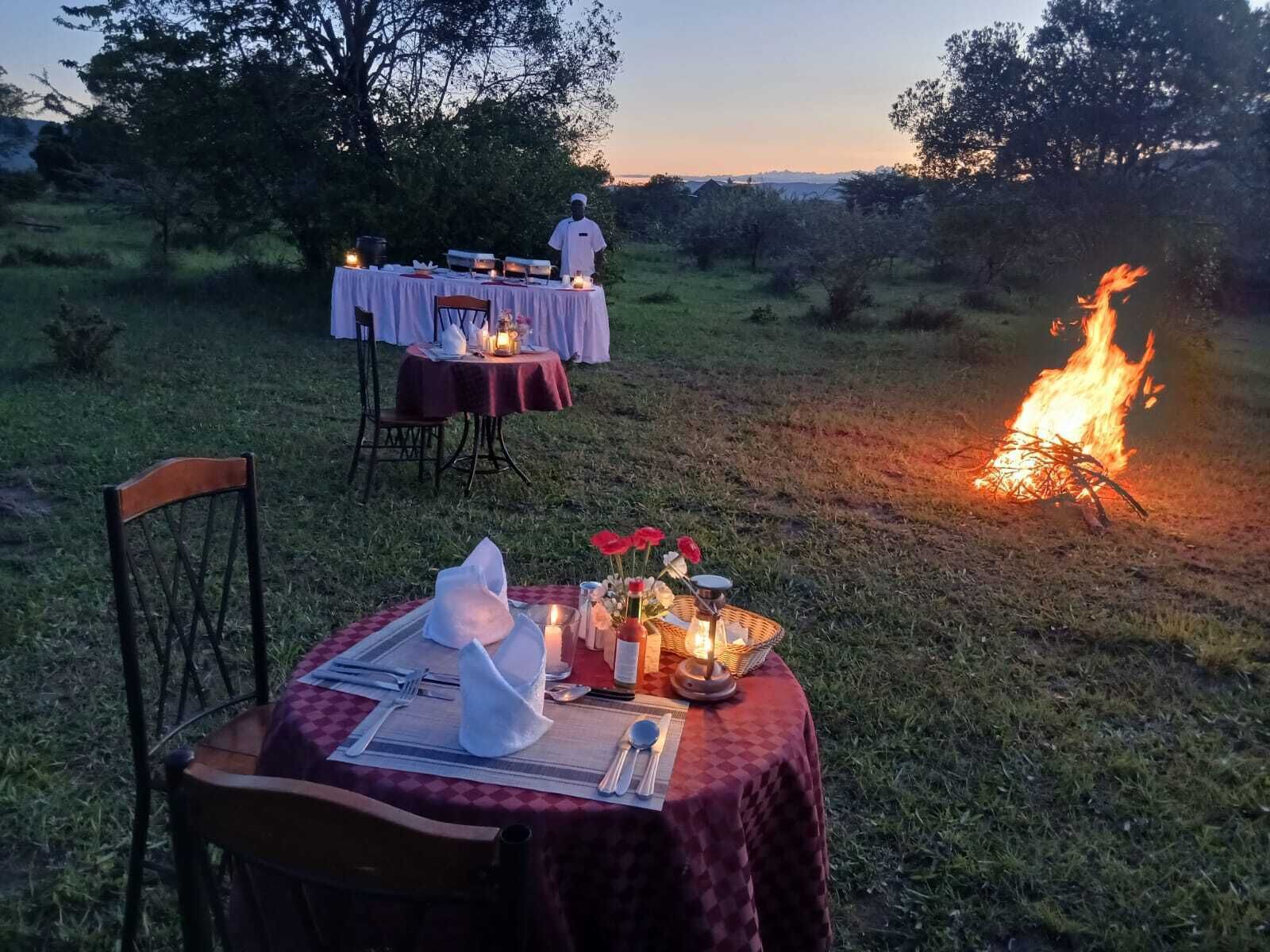 Un área de comedor al aire libre con mesas dispuestas para una comida, una chimenea y un chef al fondo.