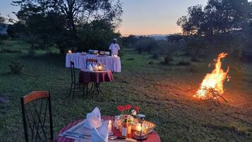 Un área de comedor al aire libre con mesas dispuestas para una comida, una chimenea y un chef al fondo.