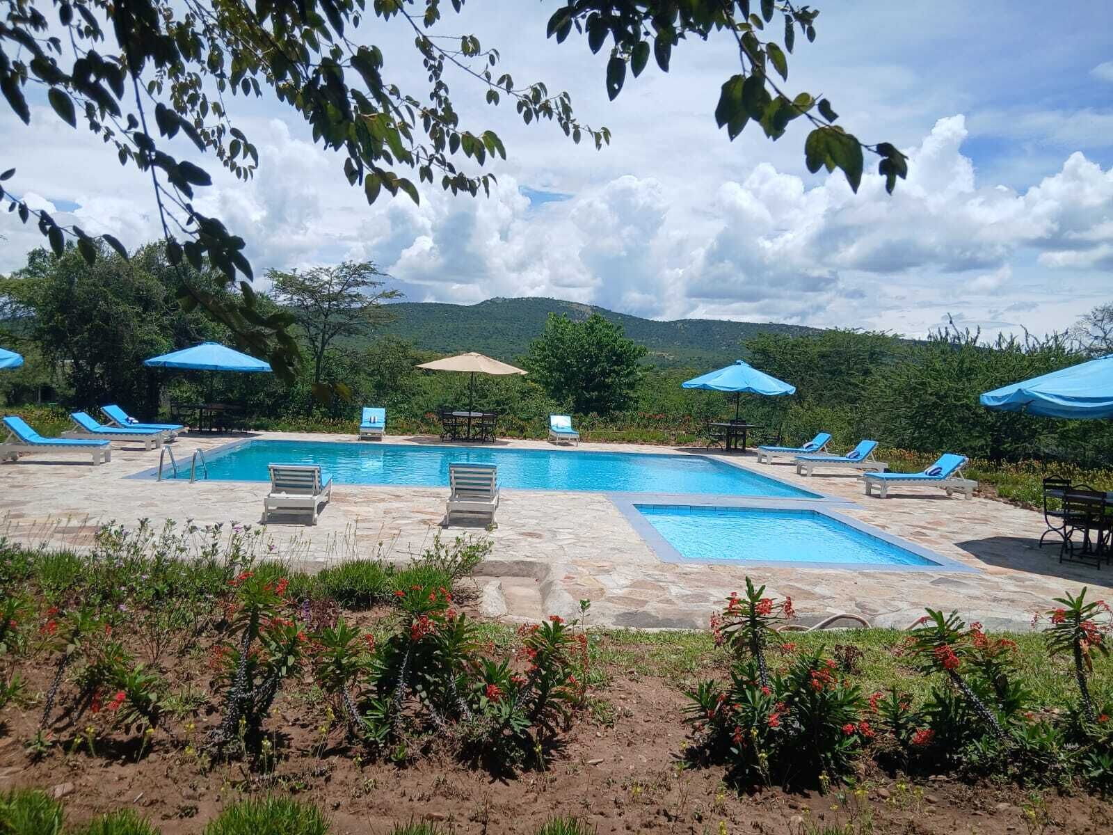 Uma área de piscina com espreguiçadeiras e guarda-sóis, rodeada por vegetação e montanhas.
