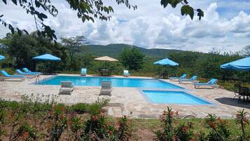 Uma área de piscina com espreguiçadeiras e guarda-sóis, rodeada por vegetação e montanhas.
