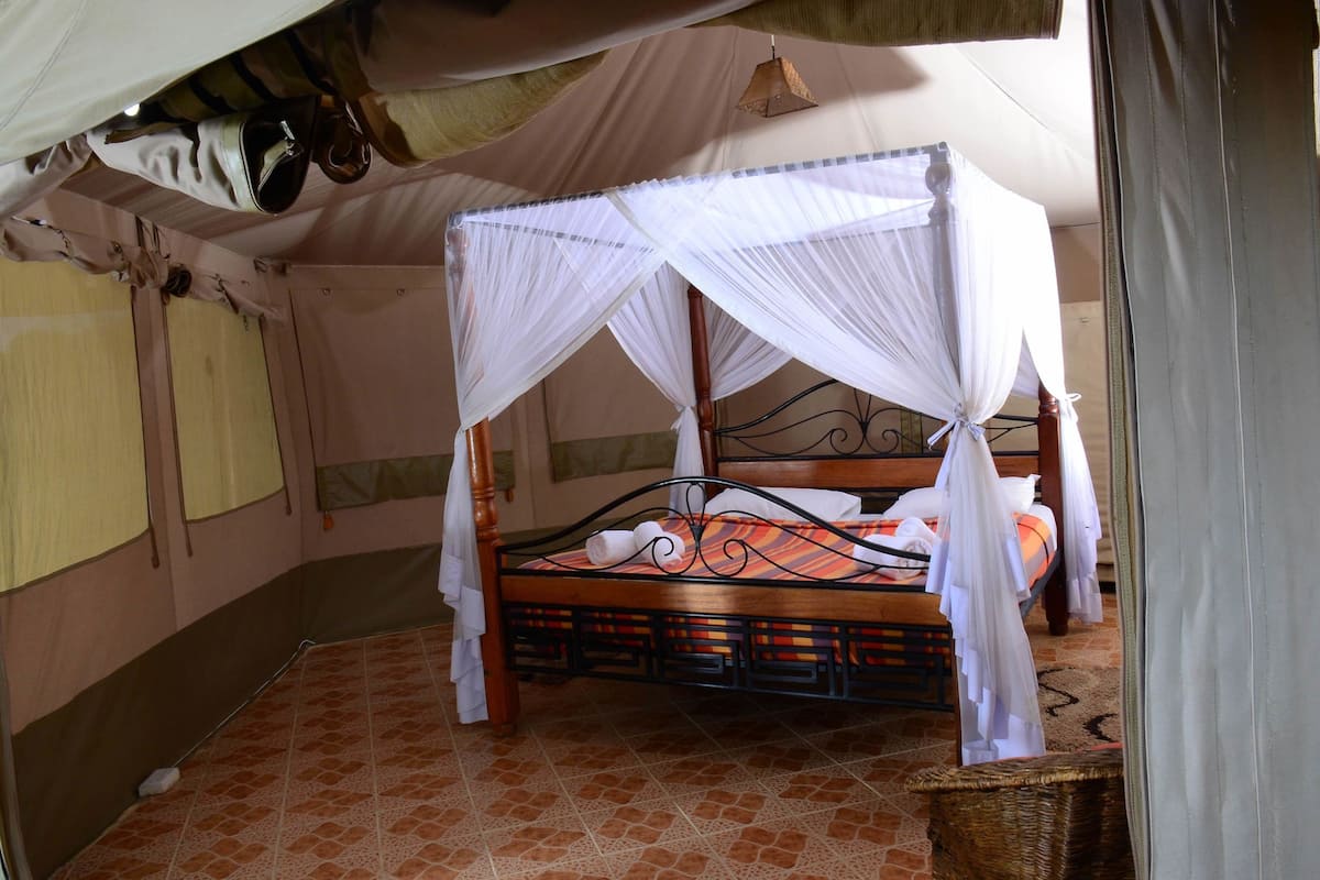 A four-poster bed with a canopy, a wooden headboard, and a patterned floor.