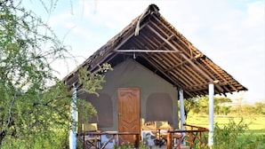 A rustic cabin with a thatched roof, a wooden door, and a porch with benches.