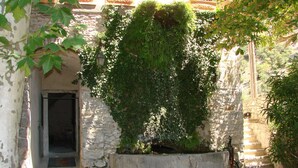 A stone building with a door and a small garden area with a concrete planter. - Domaine de la Carrière (Sumene)