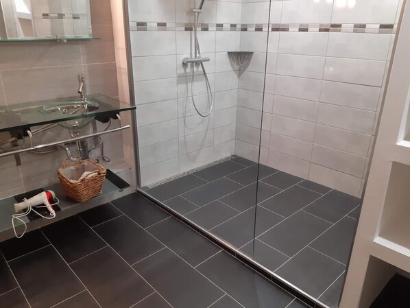 A modern bathroom with a glass shower enclosure, a glass sink, and a dark tiled floor. - Domaine de la Carrière (Sumene)