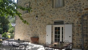 A stone building with a patio area featuring outdoor furniture and a table. - Domaine de la Carrière (Sumene)