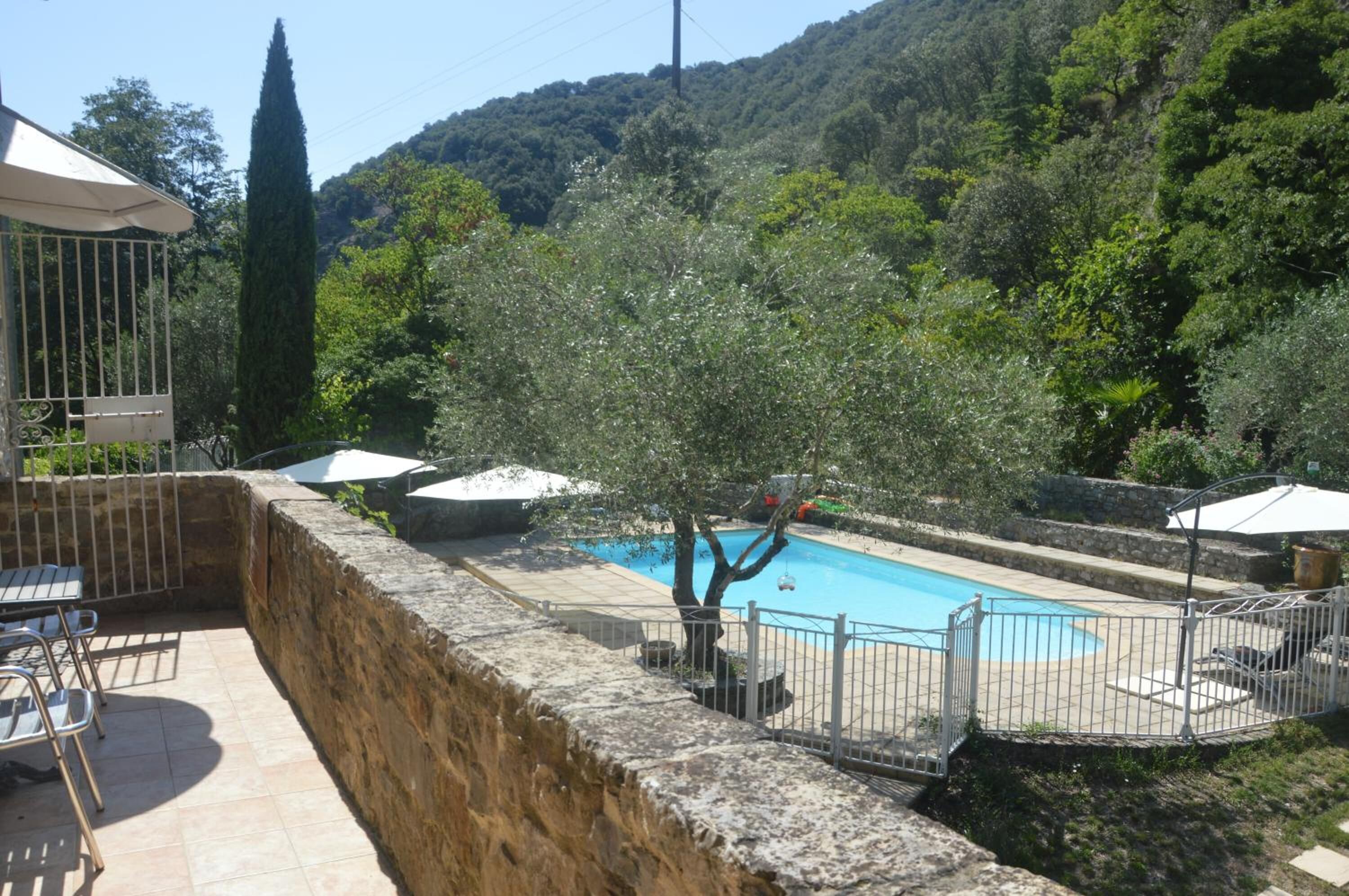 Une piscine entourée d’un mur de pierre, agrémentée de mobilier d’extérieur et de parasols.