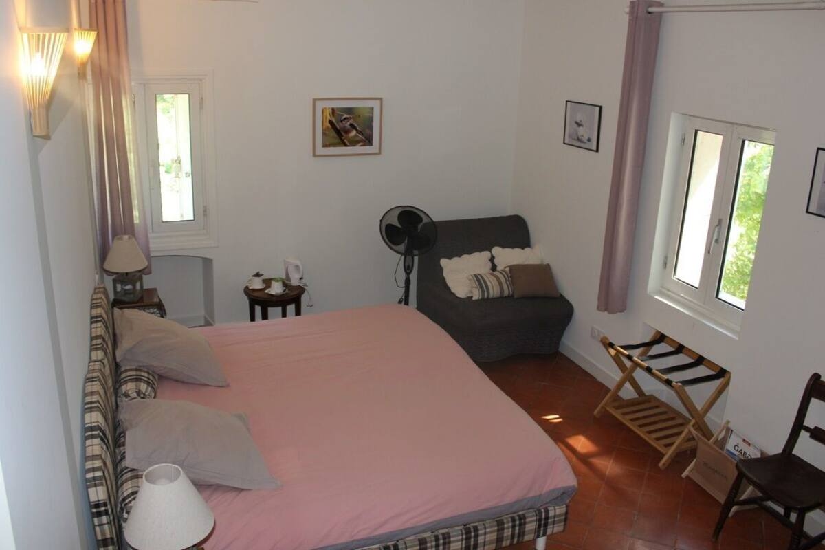 Een slaapkamer met een bed, een stoel, een ventilator en een raam.