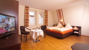 Een hotelkamer met een bed, een televisie, een tafel met stoel en een raam met gordijnen.