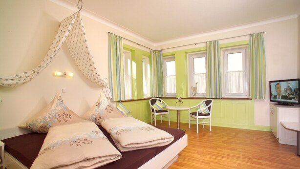 Een slaapkamer met een bed, een hangend hemeltje, een kleintje tafel met stoelen en een televisie.