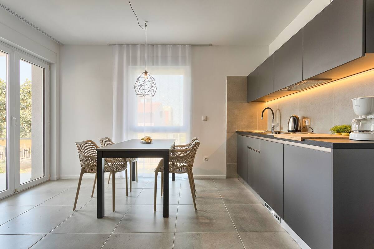 A modern kitchen with a dining area, large windows, and a pendant light.