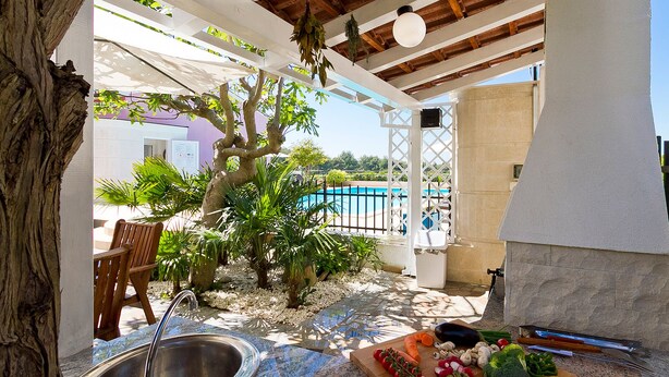 Un espace extérieur abrité comprenant une piscine, un banc en bois et une variété de légumes frais disposés sur une planche à découper.