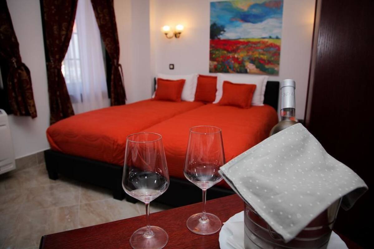A hotel room with a bed, two wine glasses, and a bottle on a table.