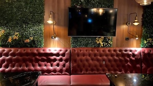 Un rincón acogedor con un banco rojo acolchado, un televisor de pantalla plana montado en una pared de madera y dos lámparas de pared.