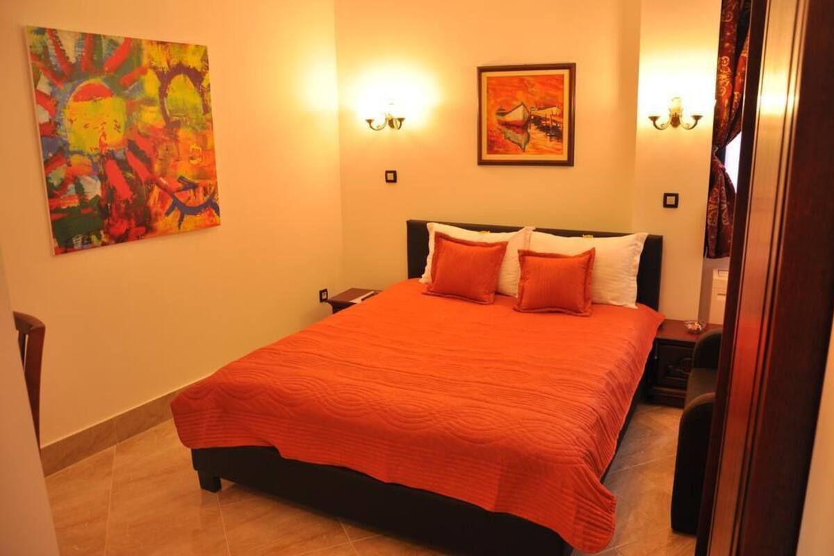 A bedroom with a large bed, two bedside tables, a nightstand, a painting on the wall, and a lamp.