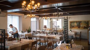 A restaurant with multiple tables set for dining, a waiter attending to a table, and a large painting on the wall. - Postojna Cave Rooms & Apartments Proteus (Postojna)