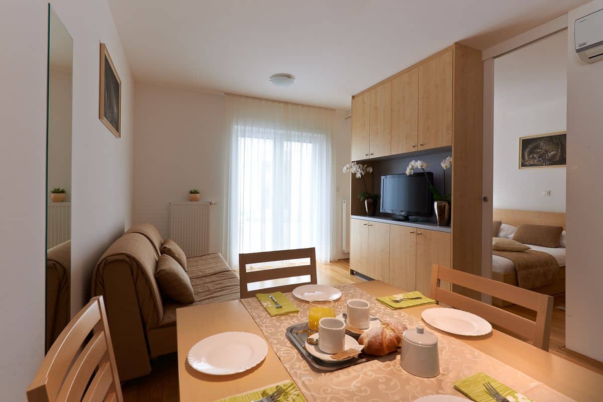 A cozy dining area with a table set for four, a sofa, and a television in the background.