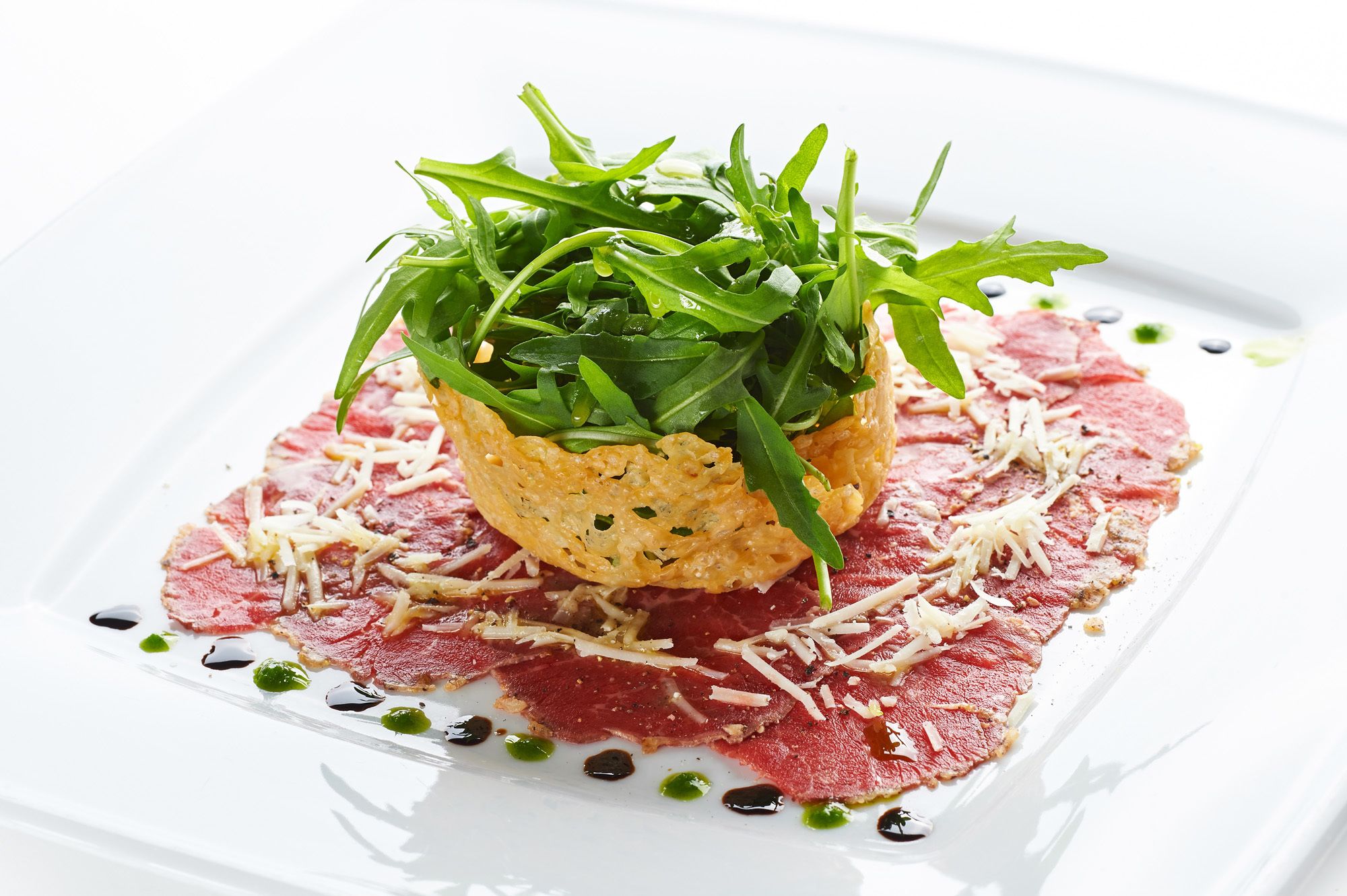Ein Gericht mit Rucola und geriebenem Käse auf einem Teller mit roter Soße.