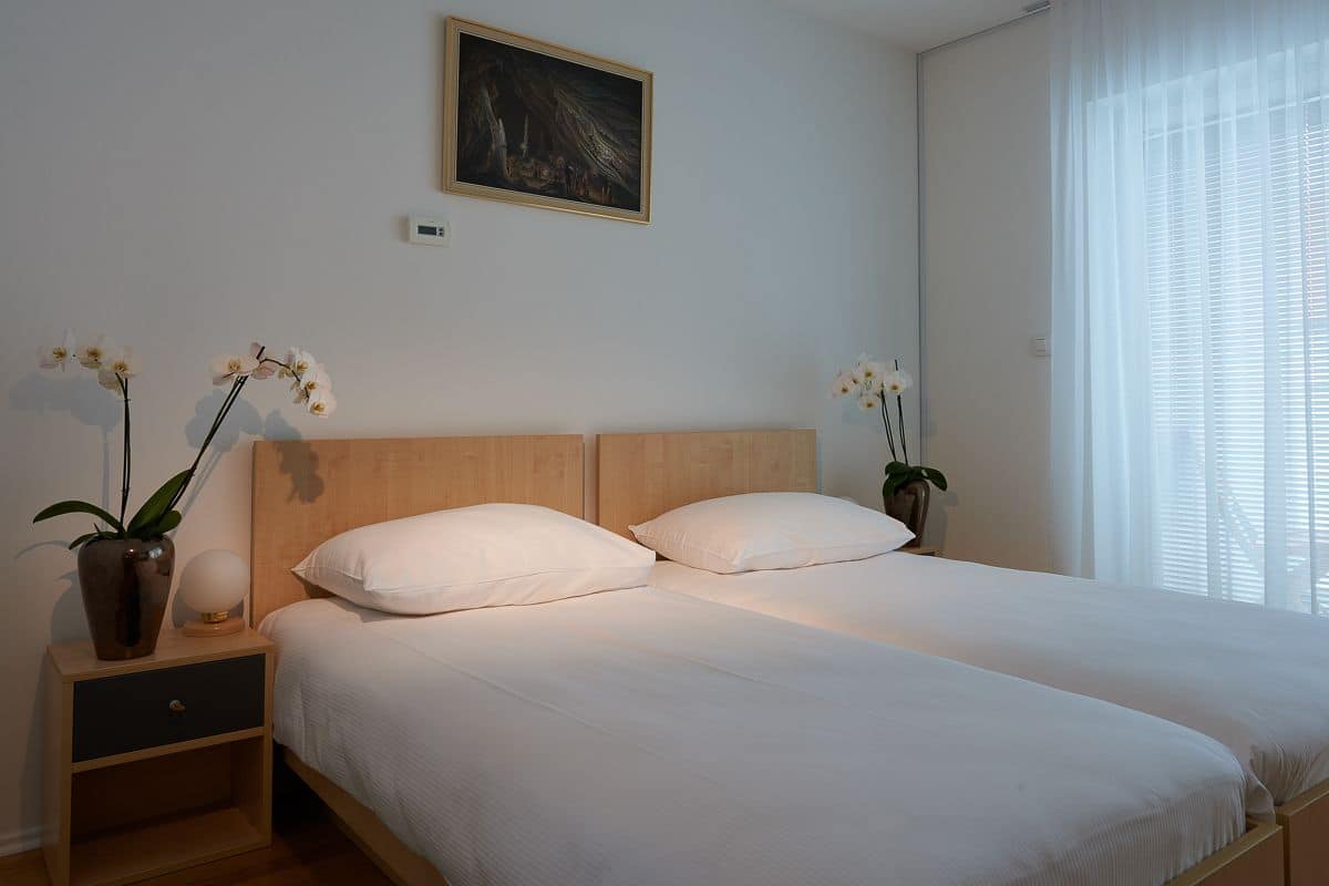 A bedroom with a wooden headboard, two white pillows, a bedside table with a vase of flowers, and a painting on the wall.