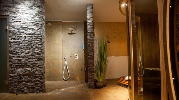 Une salle de bain moderne avec des murs en pierre, une douche et un espace délimité par des parois de verre.
