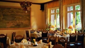 A dining area with round tables set for a meal, wooden chairs, a chandelier, and a large painting on the wall. - Gasthaus Wagner (Golzow)