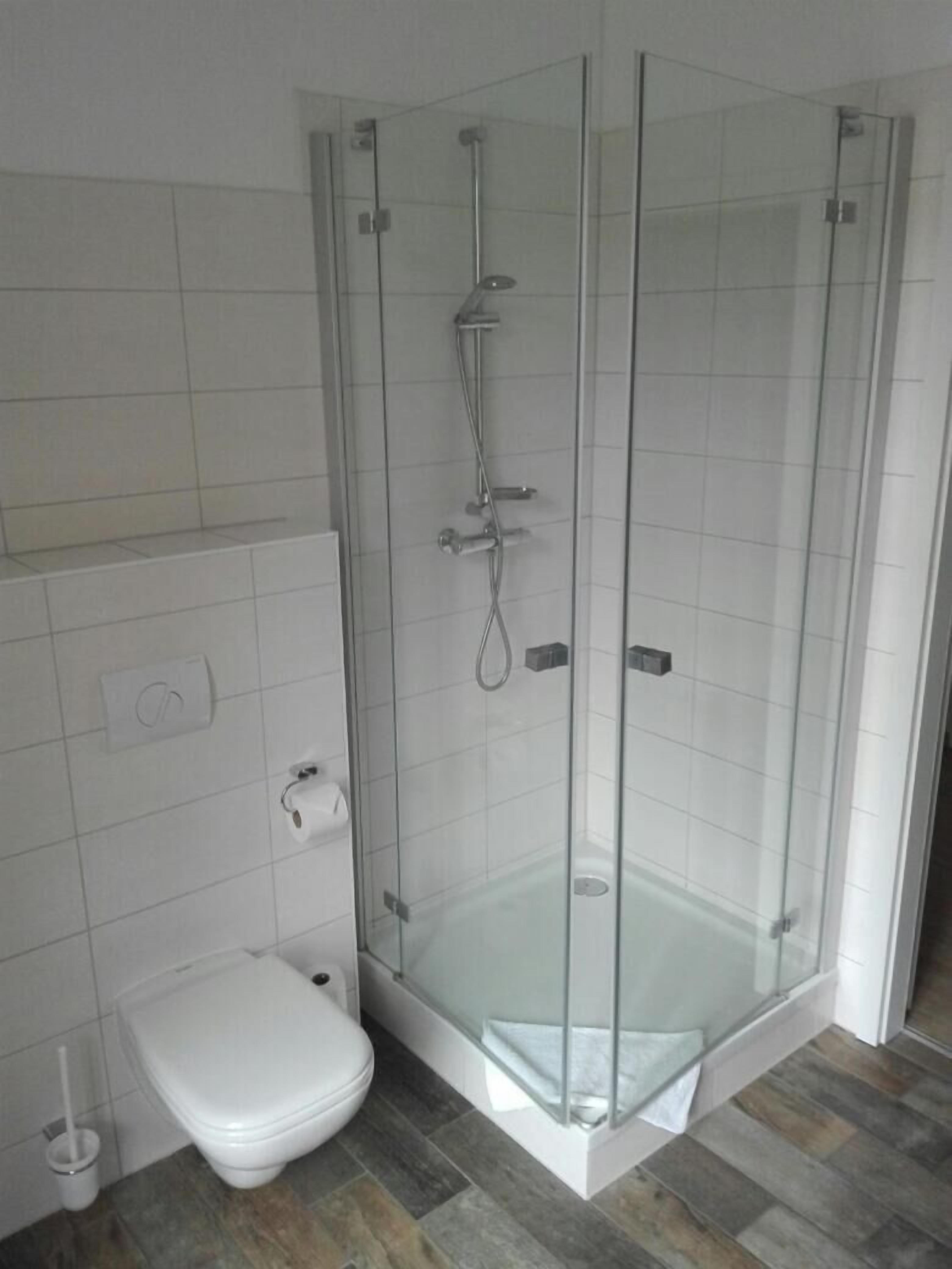 Een moderne badkamer met een douche met glazen wand, een wit toilet en een betegelde vloer.