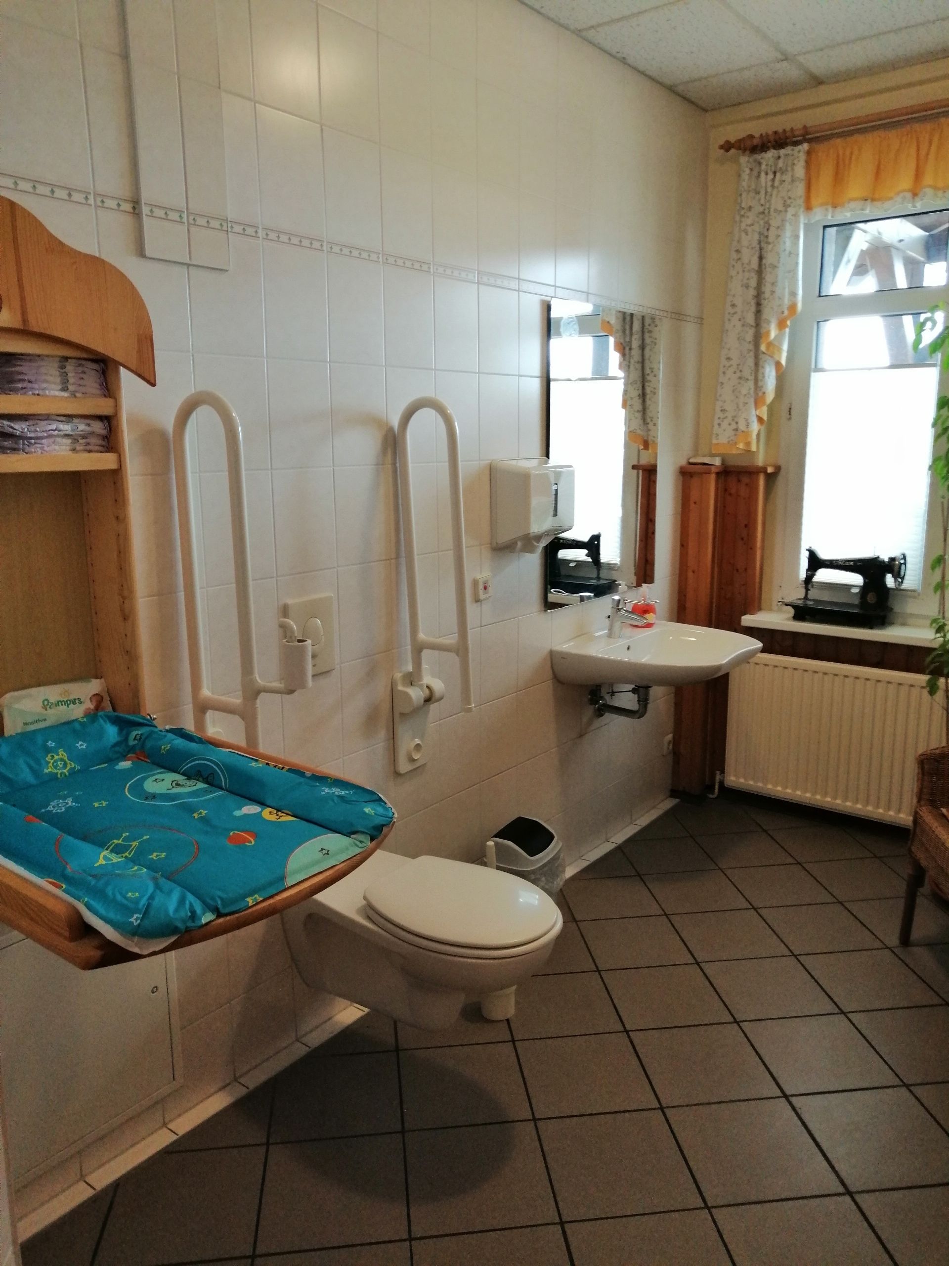 Un baño con inodoro, bidé, lavamanos y una ventana con cortinas.