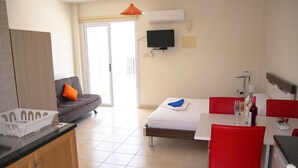 Una habitación de hotel moderna con sofá, cama, mesa de comedor con sillas, televisor y aire acondicionado.