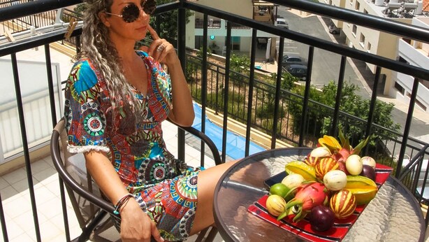 Un balcón con vistas a un paisaje urbano, una mesa con fruta y una persona sentada.