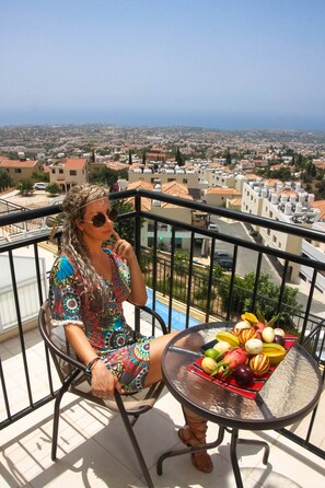 Un balcón con vistas a un paisaje urbano, una mesa con fruta y una persona sentada.