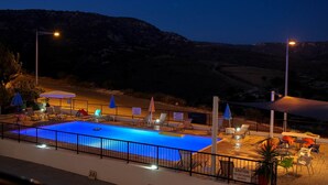 Una piscina con sillones de descanso y sombrillas, rodeada por una cerca y una vista de un paisaje montañoso.