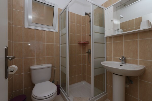 A bathroom with a toilet, a glass-enclosed shower, and a sink. - Peyia Pearl (Pegeia)