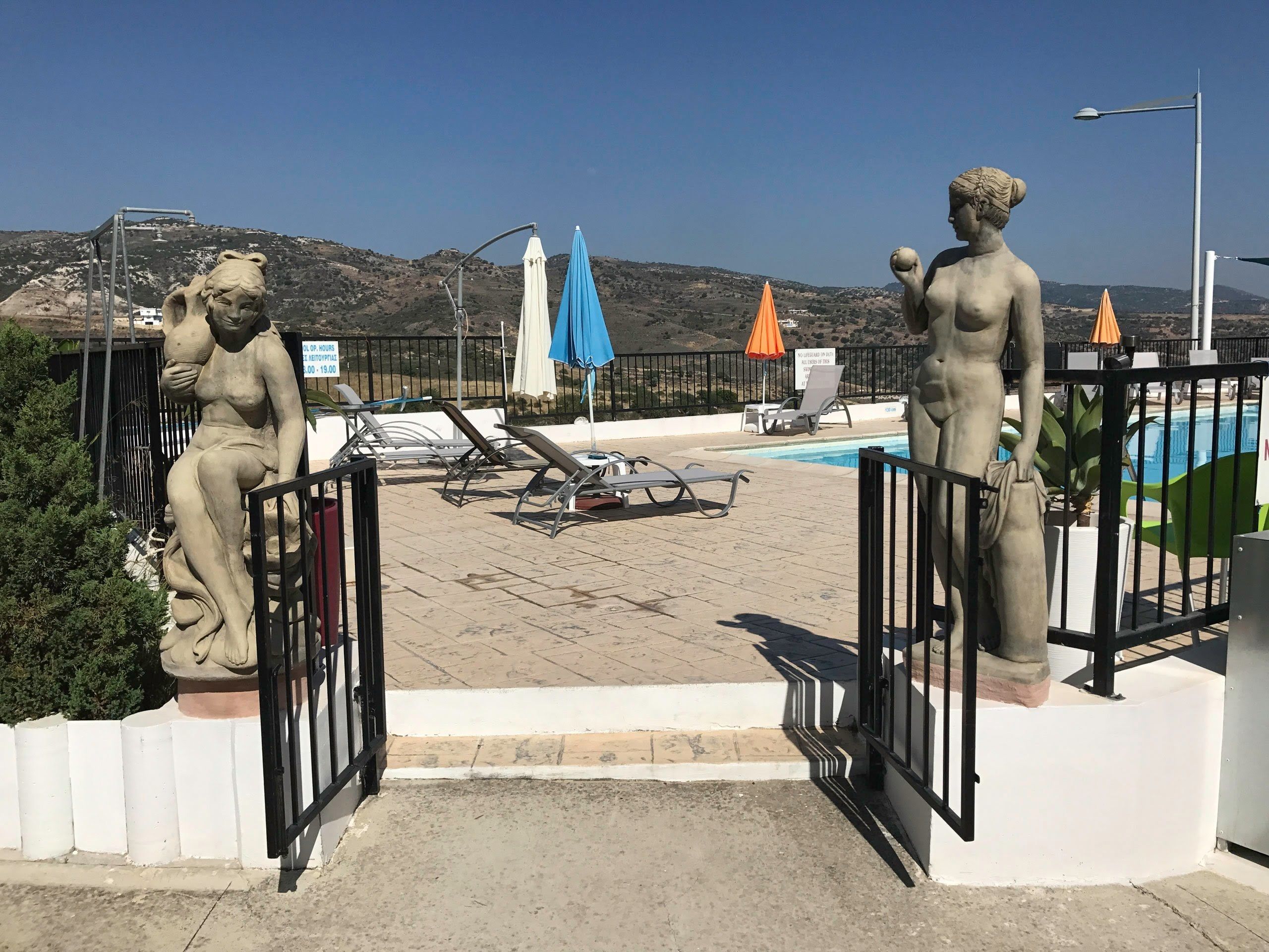Ein Poolbereich mit zwei Steinfiguren, Liegestühlen und Sonnenschirmen.
