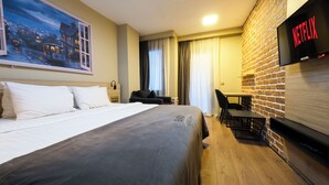 Habitación de hotel con cama, escritorio, silla, televisor mostrando 'NETFLIX' y pared de ladrillo.