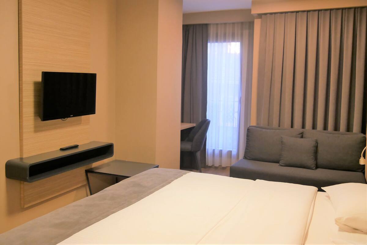 Une chambre d’hôtel avec un lit, un téléviseur fixé au mur, un bureau et un canapé.