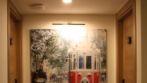Un pasillo con un cuadro grande enmarcado de un tranvía en la pared, puertas de madera y piso de baldosas.