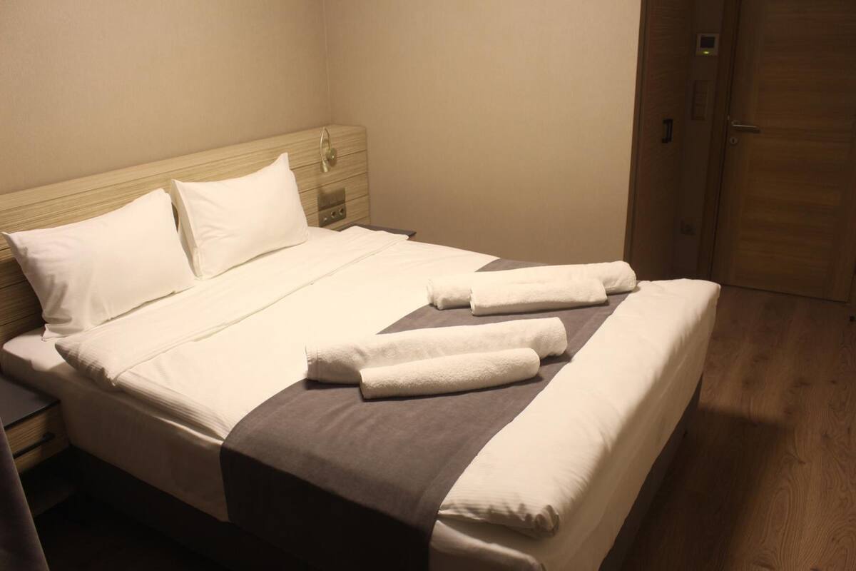 Un lit bien fait, avec du linge de lit et des serviettes blanches, une tête de lit en bois et un plancher en bois.