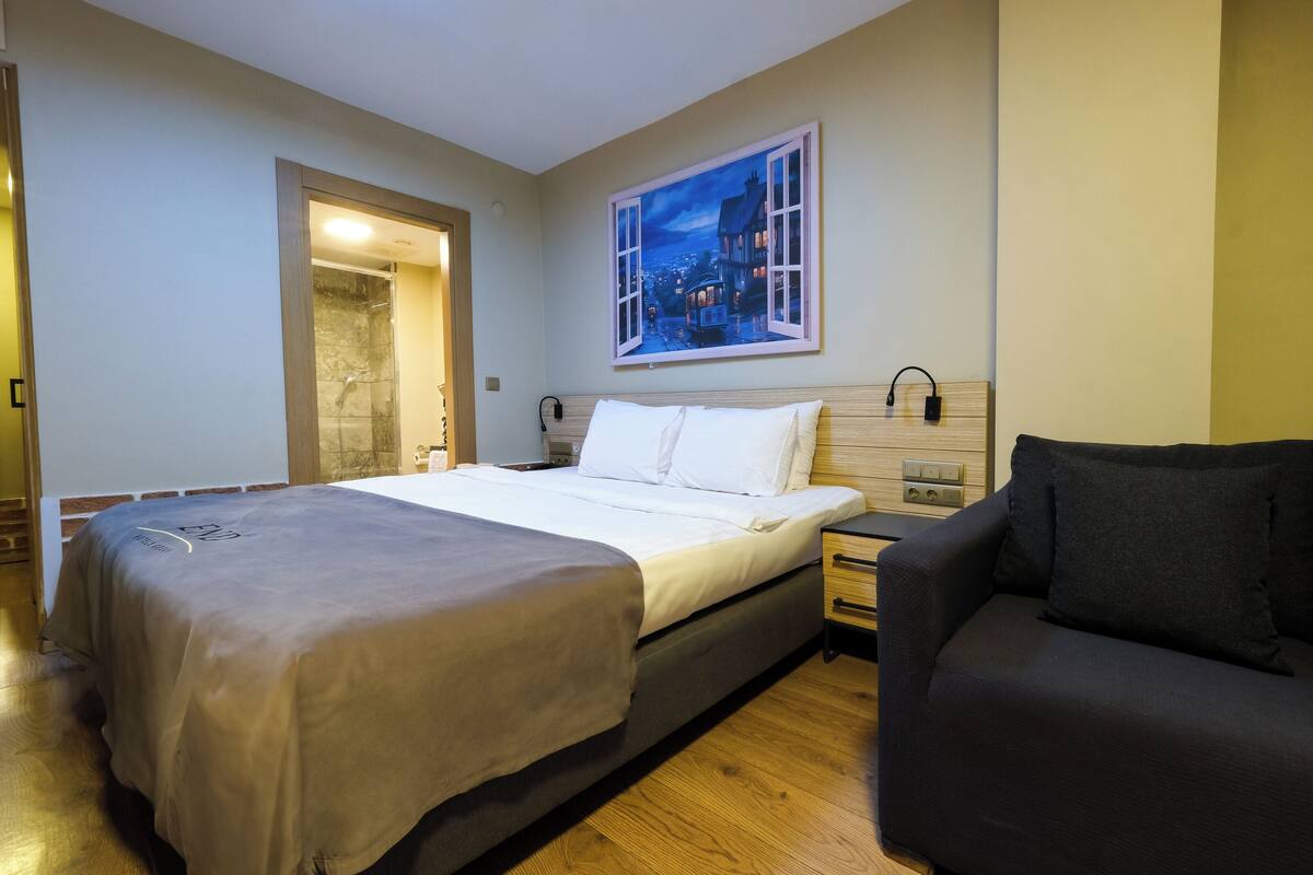 Une chambre d’hôtel comprenant un lit, une table de chevet, une chaise, un tableau représentant une scène nocturne et un espace douche.