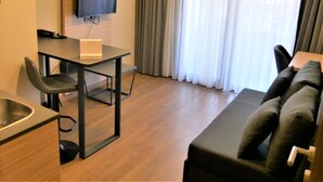 Una sala moderna con un sofá, una mesa de comedor con sillas, un televisor montado en la pared y un ventanal con cortinas.