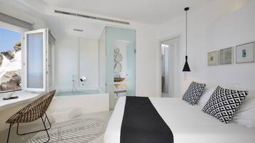 Un dormitorio moderno con una cama grande, una ventana con vista a rocas, una bañera y una silla junto a la ventana.