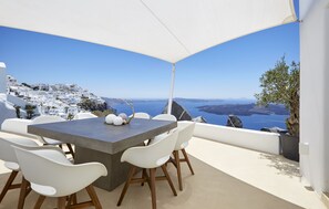 A terrace with a table and chairs, overlooking a coastal landscape with white buildings and a view of the sea. - Villa Etheras (Santorini)