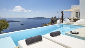 Ein Poolbereich mit Meerblick, eine Person steht am Pool und Liegestühle mit Handtüchern sind bereitgestellt.