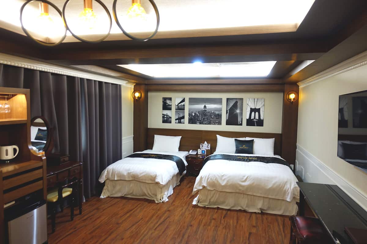 A hotel room with two beds, a desk, a chair, a mirror, and a wall with framed pictures.