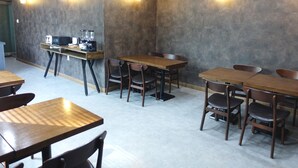 A modern cafe with wooden tables and chairs, a coffee machine, and wall-mounted lights. - Prince Hotel (Goseong)