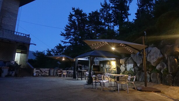 An outdoor patio area with tables and chairs, a barbecue grill, and string lights. - Prince Hotel (Goseong)
